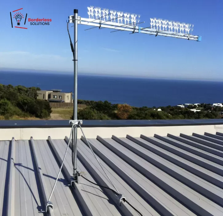 TV antenna mast mounted on coastal rooftop with tripod base and RG6 cabling - Borderless Solutions licensed antenna installation overlooking ocean