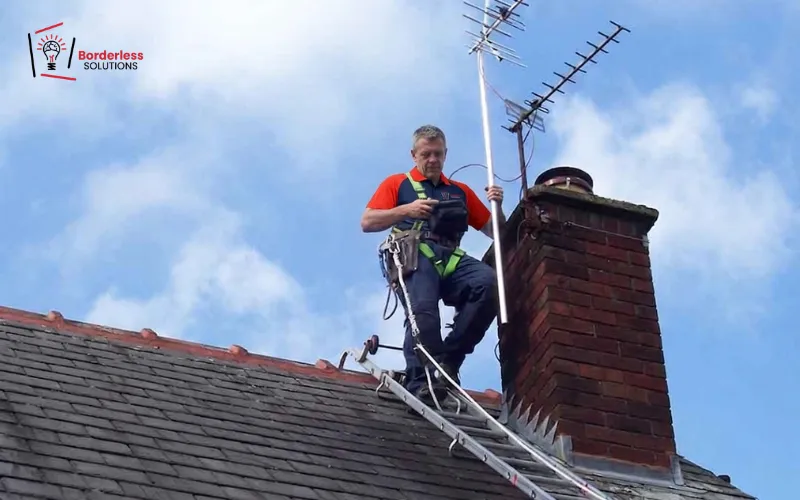 Technician installing UHF TV antenna on chimney rooftop with safety harness - high rise and infill zone reception setup