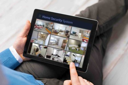A person monitors their home security system through a tablet displaying multiple indoor CCTV feeds. Borderless Solutions provides smart home security system installation across Melbourne, enabling residents to protect and monitor their property remotely with real-time access, motion alerts, and smart device integration.